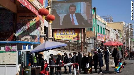 Residents walk through a security checkpoint and past a screen showing Chinese President Xi Jinping in Hotan, Xinjiang, on November 3, 2017.